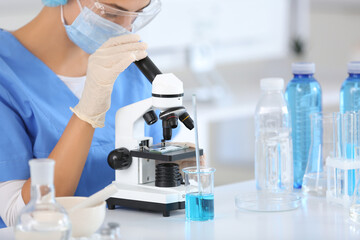 Female young scientist with microscope and professional glassware examining water quality in research laboratory, closeup