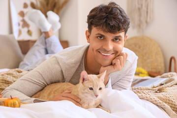 Wall Mural - Young man with cute cat lying in bedroom on autumn day