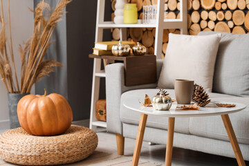 Cup of tea with fir cones, decorative pumpkin and autumn leaves on table in living room