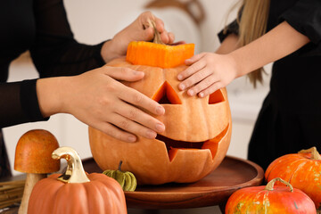 Sticker - Little girl with her mother dressed as witches carving Halloween pumpkin in kitchen, closeup