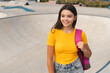© InsideCreativeHouse - Latin hispanic positive high school pupil student teen girl teenager female skater in casual t-shirt with bag spend time weekend summer holidays in skate park after lessons looking aside copy space