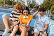 © InsideCreativeHouse - Group of smiling friends teenagers high school pupils college students watching funny video laughing out having fun using gadgets internet phones handing out in sport court yard outside