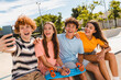 © InsideCreativeHouse - Happy smiling group of teenagers high school pupils friends classmates college students boys girls with bags hanging out take selfie shot picture photo having fun in skate park sitting on ramp outside