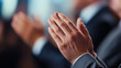 © Kateryna - A close-up of hands clapping in a diverse audience at a formal event. The people are dressed in business attire, showing a moment of collective appreciation and recognition during