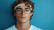 ©  Dreamy Shots - Close-up portrait of a young man wearing glasses and headband, standing against a bright blue wall background, modern casual style, serious expression, trendy eyewear, athletic look