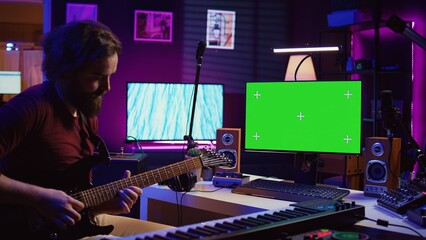 Leinwandbilder - Male singer learning to play a new song on acoustic guitar, using greenscreen on computer to watch online video tutorials. Artist songwriter practicing with his instrument in home studio. Camera B.