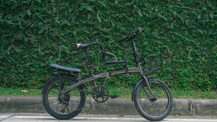 Close-up view of a folding bike parked beside a leafy wall, showcasing its compact design against a green, urban landscape