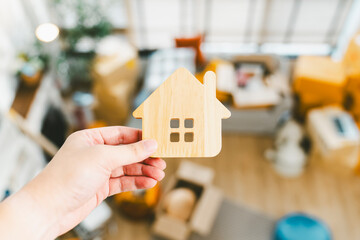 A moving company employee holds a miniature house model with blur items being moved into the house are scattered around.