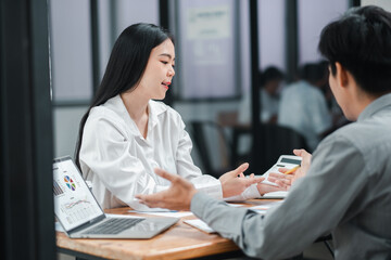 Wall Mural - Two colleagues engaged in a business discussion at a modern office table with laptops and charts.