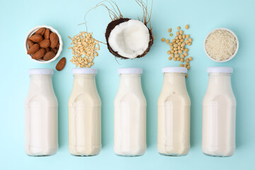 Wall Mural - Different types of vegan milk in bottles and ingredients on light blue table, flat lay