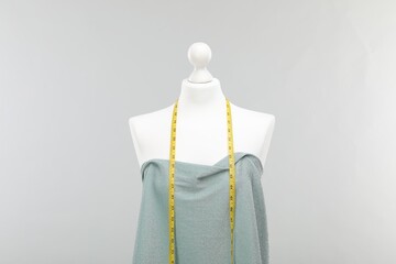 Poster - Mannequin with measuring tape and fabric against light grey background. Creating new outfit