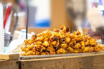 A pile of food on a wooden table. The food is cooked and looks delicious. The table is covered with a lot of food, and it is a buffet