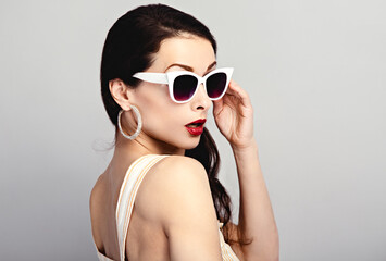 Fashion studio closeup portrait of gorgeous elegant surprising woman in white sunglasses and fashion earrings posing on blue wall background with empty copy space