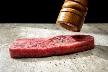 A piece of sirloin meat is being flavored with a pepper mill