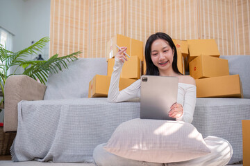 Wall Mural - Young Entrepreneur Selling Products Online from Home Using Tablet with Cardboard Boxes in Background