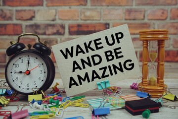 Wake Up And Be Amazing text on paper card with alarm clock and stationary on wooden background