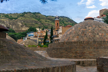 Sticker - Domes of sulfur baths and Tbilisi Mosque (Juma Mosque) in the downtown. Mountains and sky with clouds in the background