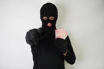 Wall Mural - Dangerous young Adult black masked robber is holding a bunch of indonesian money after stealing from his victim.