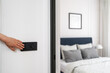 © brizmaker - Hand reaching for light switch near a cozy bedroom at home during daylight
