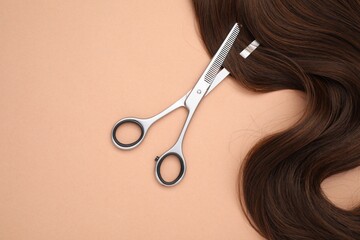 Wall Mural - Brown hair strand and professional scissors on pale coral background, top view