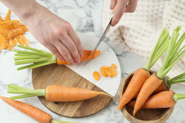 woman cutting fresh carrot at white marble table, top view