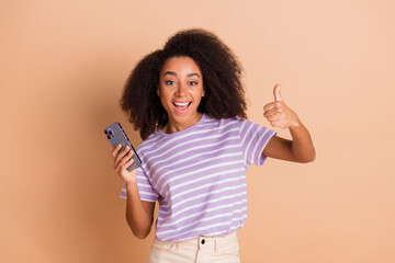 Poster - Photo of pretty young woman smart phone thumb up wear striped t-shirt isolated on beige color background