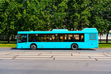 Blue bus side view on the road in city green trees street