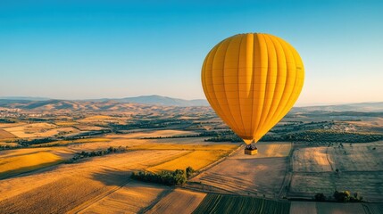 aerial view of a bright yellow hot air balloon floating over a patchwork of fields, with a clear blu