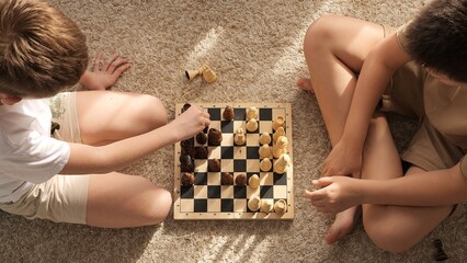 Two kids playing chess on the floor, focused on chessboard. Chess game captures their attention, highlighting strategy and concentration. Perfect for themes of childhood, chess learning, and strategy.