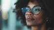 © JoxyAimages - Close-up portrait of a woman with dark curly hair and glasses, gazing thoughtfully to the side, portraying introspection and calmness, against a softly blurred background.