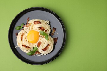 Wall Mural - Delicious pasta Carbonara with egg yolk, bacon and basil on green table, top view. Space for text