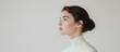 © Evgeniya - Side profile of a young woman with dark brown hair in a bun, dressed in a white high-neck top, against a soft background.