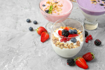 Poster - Different tasty yogurts with fresh berries and granola in glass dessert bowls on gray textured table, closeup. Space for text