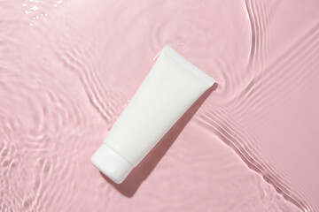 Wall Mural - Cosmetic product. Tube with cream in water on pink background, top view