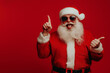 © Роман Варнава - Santa Claus brings joy in sunglasses with a fun pose against a lively red backdrop