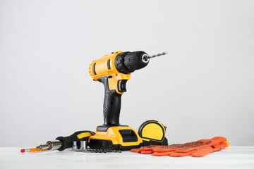 Wall Mural - Cordless electric drill, gloves, bits, screwdriver and measuring tape on white wooden table