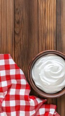 Wall Mural - A rustic wooden table features a bowl filled with creamy Greek yogurt alongside a wooden spoon, complemented by a red-and-white checkered cloth for a homey touch