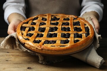 Sticker - Woman holding tasty homemade pie with blueberries over wooden table, closeup