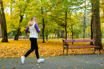 Wall Mural - Pretty middle-aged blonde woman dressed sporty running on alley full of beautiful autumnal trees in city park on autumn day. Back view. Autumnal training. Healthy running.