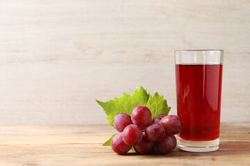 Poster - Tasty juice in glass, fresh grapes and leaf on wooden table, space for text