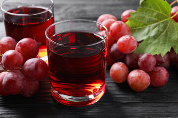 Canvas Print - Tasty grape juice in glasses, leaf and berries on black wooden table, closeup