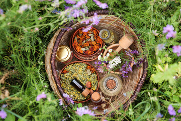 Wall Mural - Different ingredients for tincture, mortar and pestle in wicker basket on green grass outdoors, top view