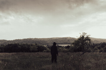 Canvas Print - A strange hooded figure, back to camera. Standing in a field in the countryside. On a moody stormy cloudy day