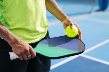 Close-up of a player's hand holding a pickleball paddle and ball on the court.