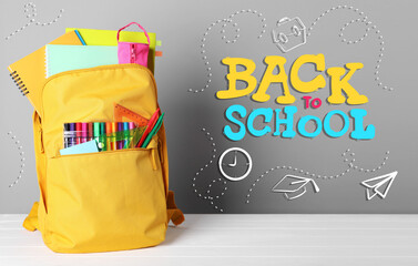 Wall Mural - Backpack with stationery on desk against grey background. Back to school