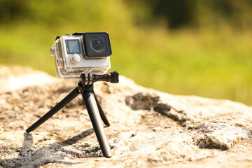 Wall Mural - Modern action camera with tripod on stone outdoors, space for text