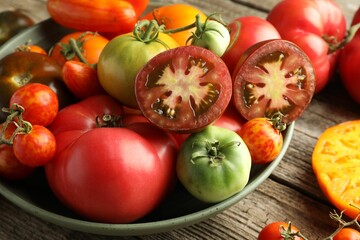 Wall Mural - Different ripe tomatoes in bowl on wooden table, closeup