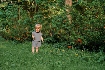 Cute Caucasian toddler child 2-years-old girl walks in a green park at sunset in summer. The concept of a joyful childhood and active pastime.