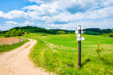 Post with cyclings routes signs on gravel road and green landscape, Suwalski Landscape Park, Podlasie, Poland