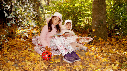 Two kids watching the book in autumn forest. High quality photo